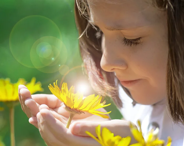 Photo of a young girl smelling flowers that thrive due to clean energy production