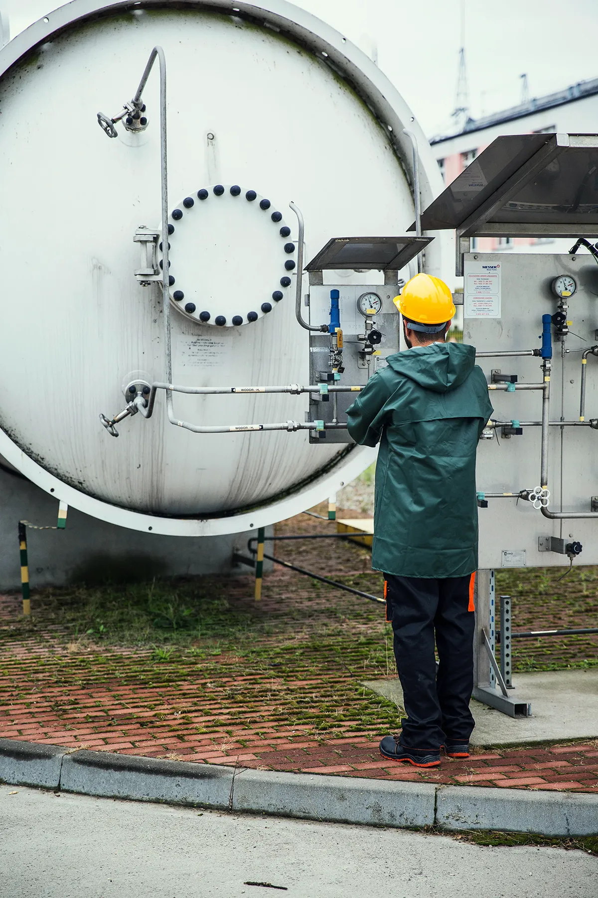 Hydrogen storage tank with a worker in a hard hat checking the pressure gauge in a potentially hazardous gas zone